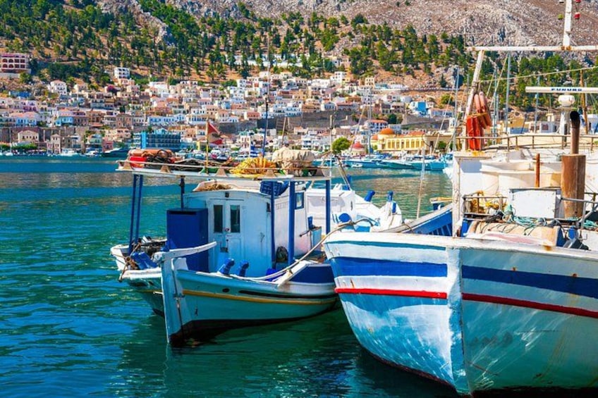 A harbor with several boats docked, a town in the background, and a hillside with buildings. 2