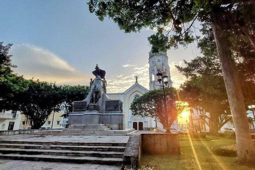 A statue on a pedestal, a church with a bell tower, and a sunset in the background. 1