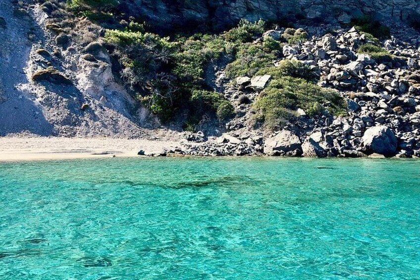 A coastal landscape with clear turquoise water, rocky cliffs, and sparse vegetation. 3