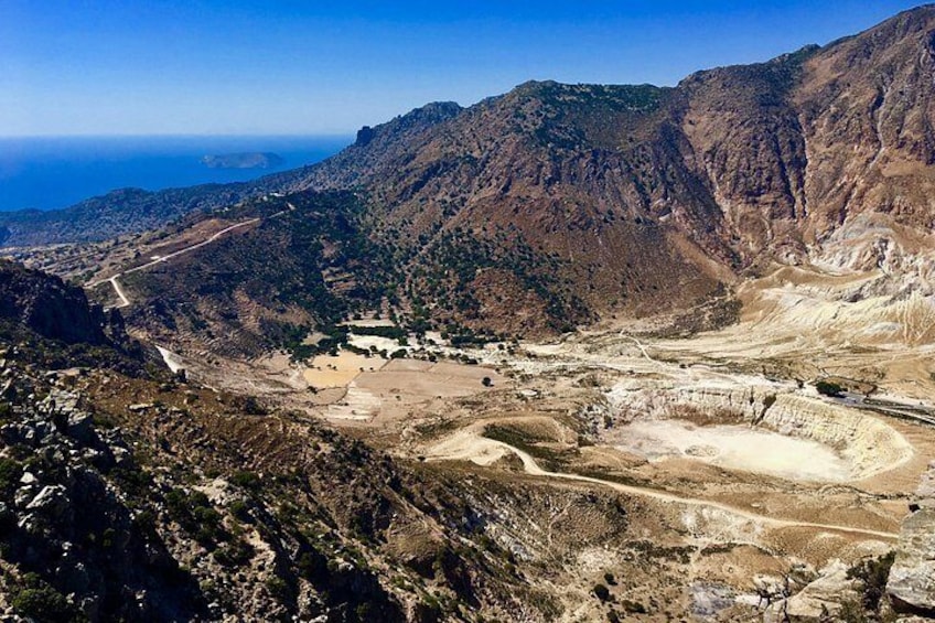 A mountainous landscape with a road winding through a valley, a small settlement, and a distant view of the sea. 2