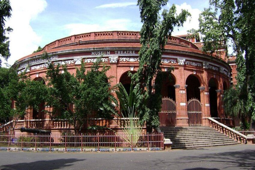 A large, circular brick building with arched doorways and a central staircase, surrounded by trees and a fence. 4