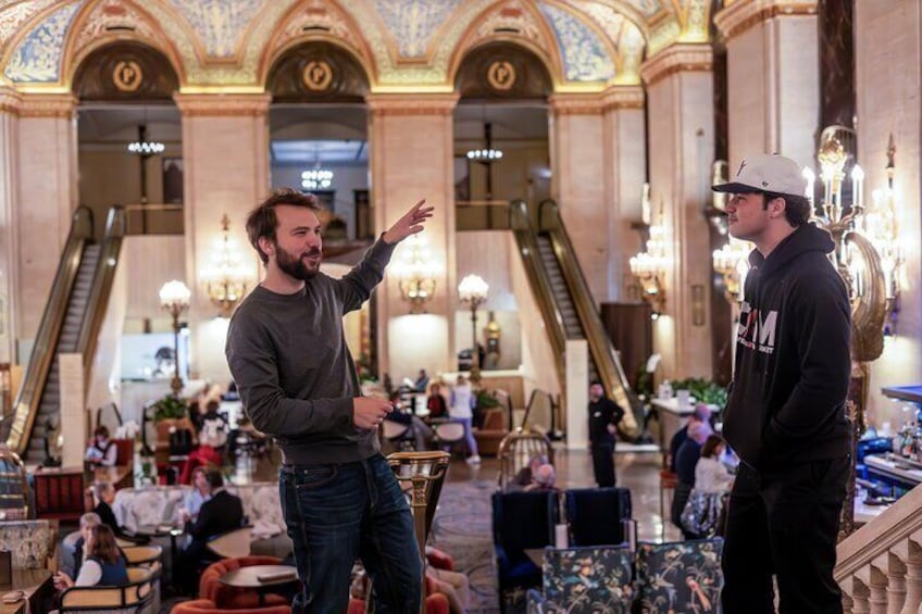 Two men conversing in a grand lobby with ornate architecture and chandeliers. 3