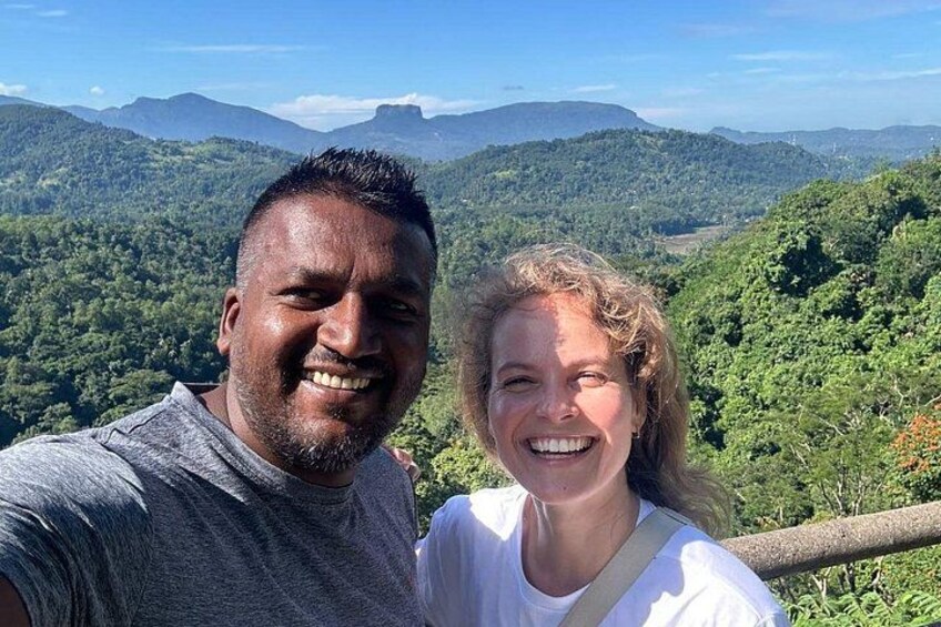 Two people standing on a hill with a forested landscape in the background. 3