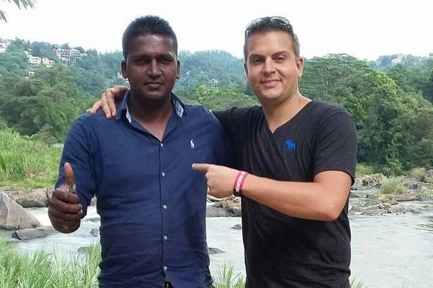 Two individuals standing by a river with greenery in the background. 2