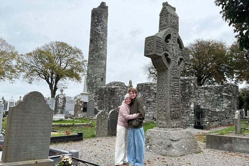 A cemetery with gravestones, a large stone cross, and a tall stone pillar. 5