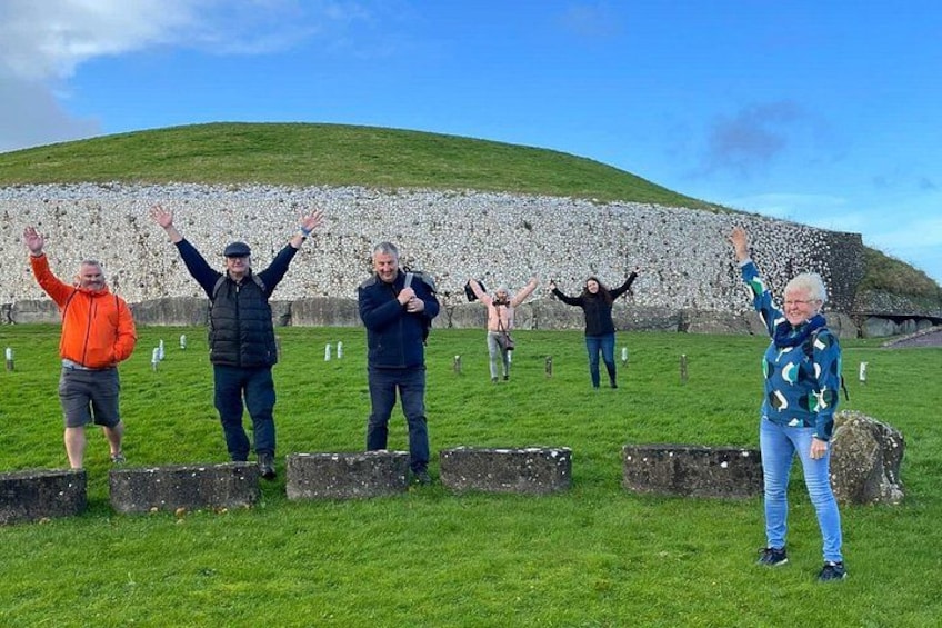 A group of people standing in a grassy field with a stone wall in the background. 1