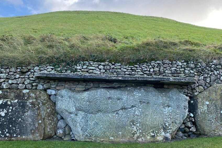 A stone wall with a flat top, surrounded by grass and a hill in the background. 2
