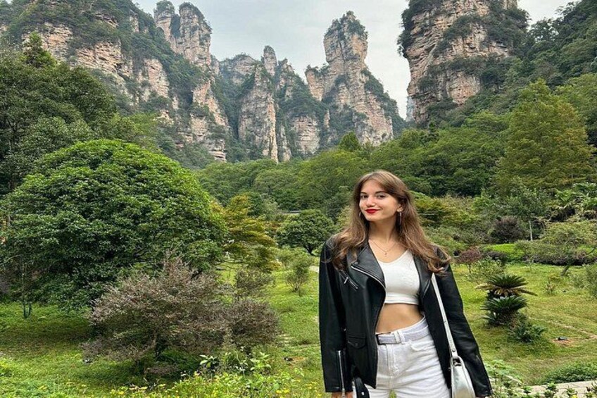 A person standing in a lush green landscape with tall, rocky cliffs in the background. 2