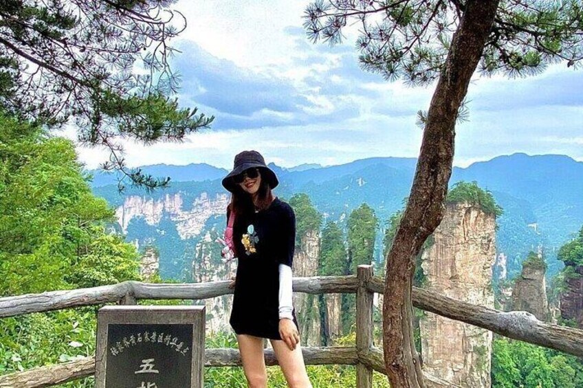 A person standing on a wooden platform with a scenic view of mountains and cliffs in the background. 5