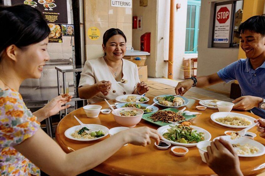 Un groupe de personnes est assis autour d’une table, devant différents plats, dans une pièce où l’on peut voir un panneau indiquant « DÉCHETS INTERDITS » et un autre panneau indiquant « ARRÊT » sur le mur. 5