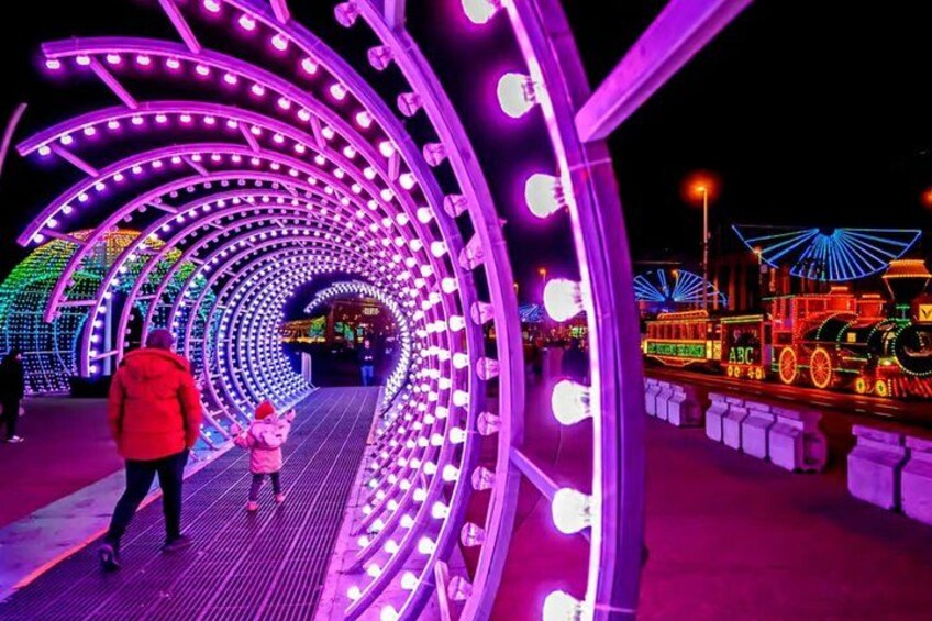 A brightly lit pedestrian walkway with a train and colorful lights. 1