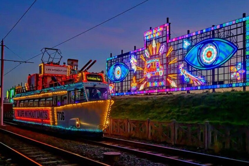 A brightly lit tram with 'Life Without Limits' and '736' on it, traveling on tracks next to a colorful illuminated wall with an eye design. 5