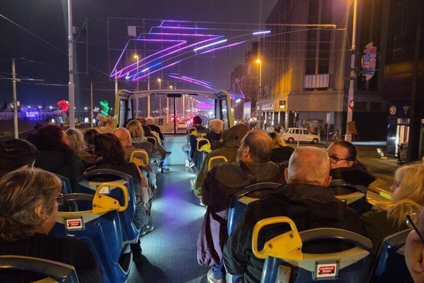 A nighttime bus with passengers seated, illuminated by neon lights. 2