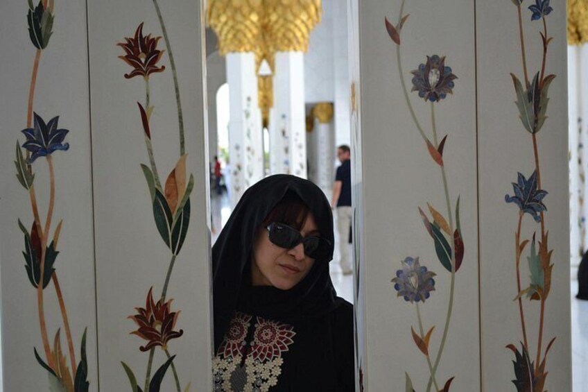 A person in a black garment with floral patterns, standing in front of a wall with vertical floral designs. 3