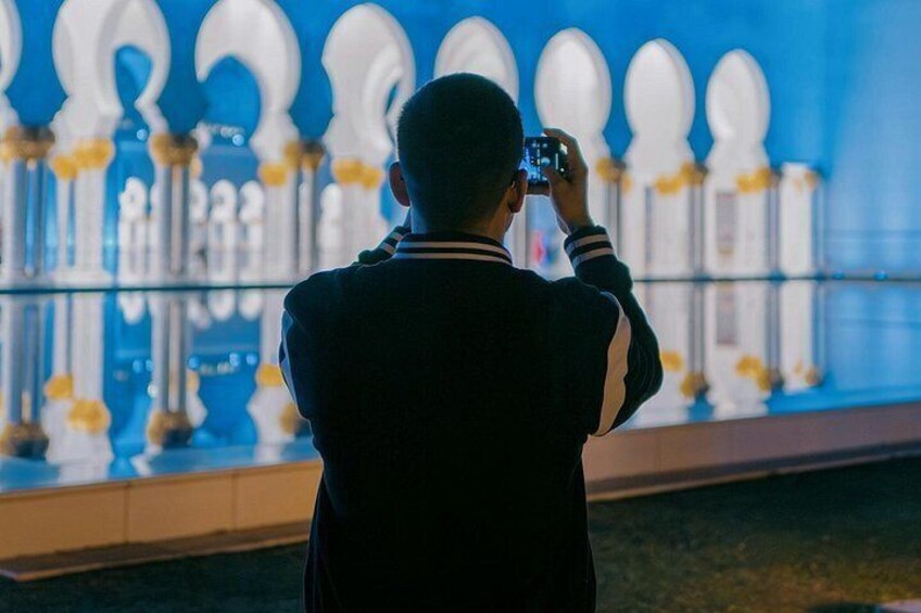 A person taking a photo of a blue-lit structure with white and yellow accents. 2