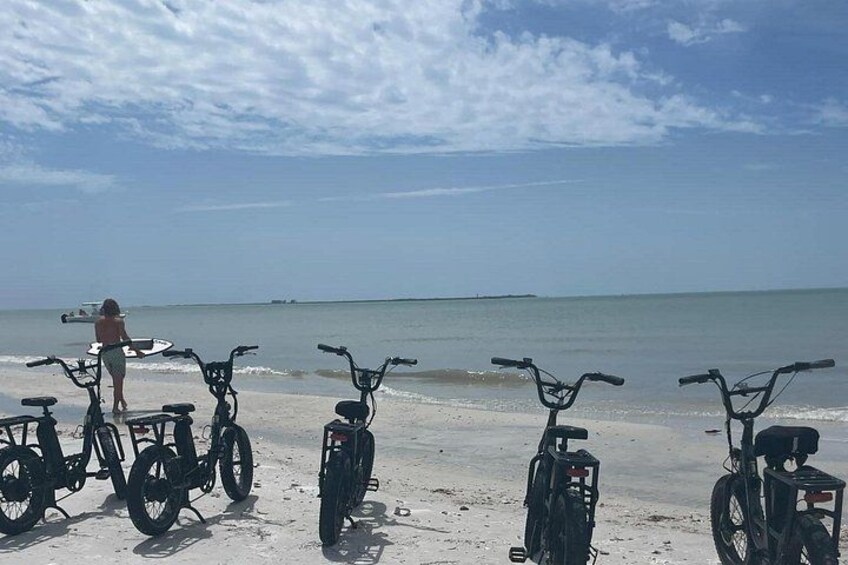 A beach with bicycles and a person with a surfboard. 2