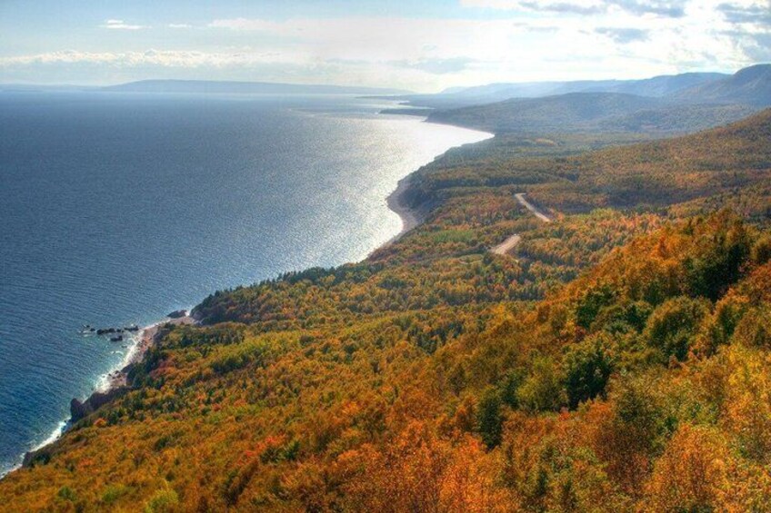 A coastal landscape with autumn foliage, a winding road, and a view of the ocean. 1