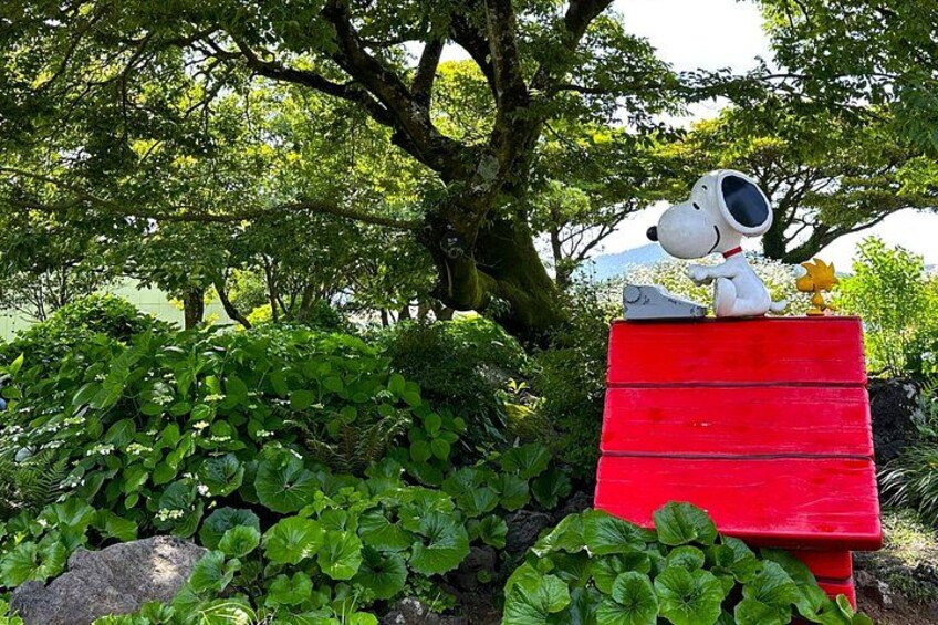 A Snoopy statue on a red bench surrounded by lush greenery. 2