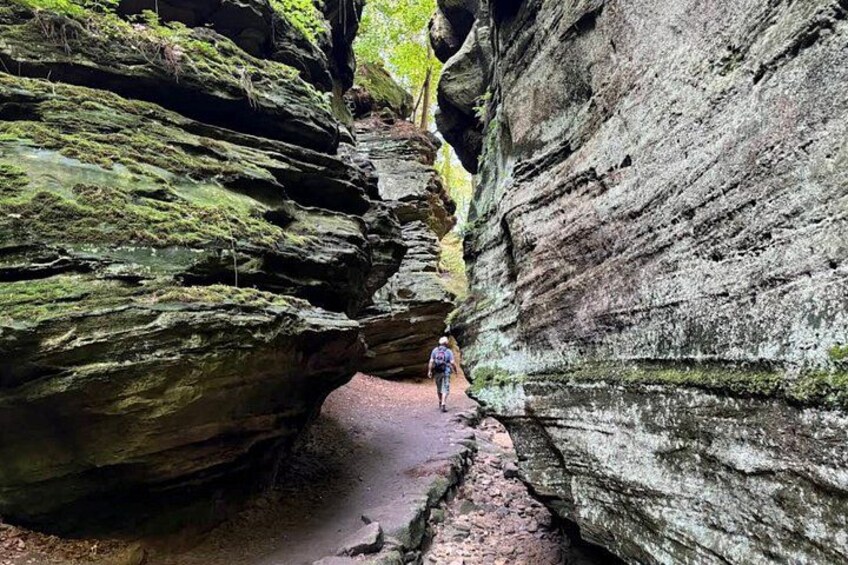 A person hiking through a narrow canyon with rocky walls and moss-covered rocks. 4