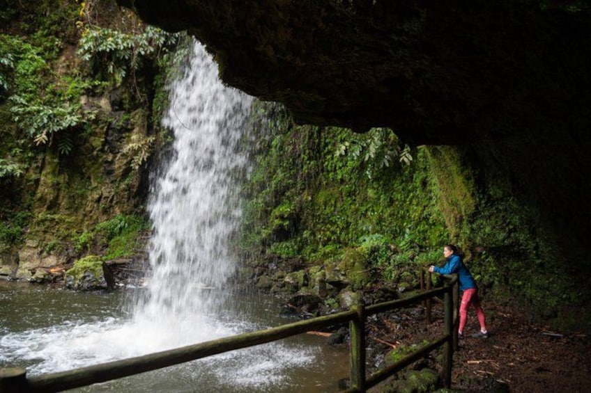 A waterfall in a forested area with a person standing on a wooden bridge. 5