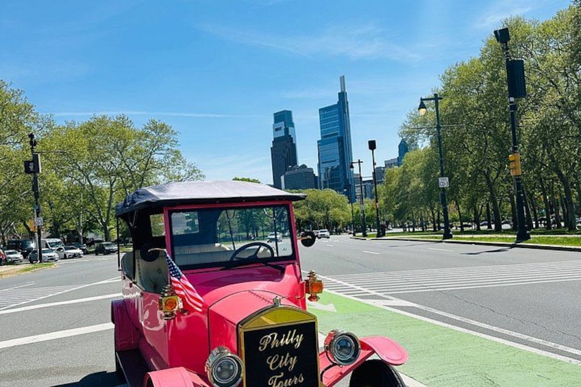 A vintage red car with an American flag on a city street with modern buildings in the background. 2