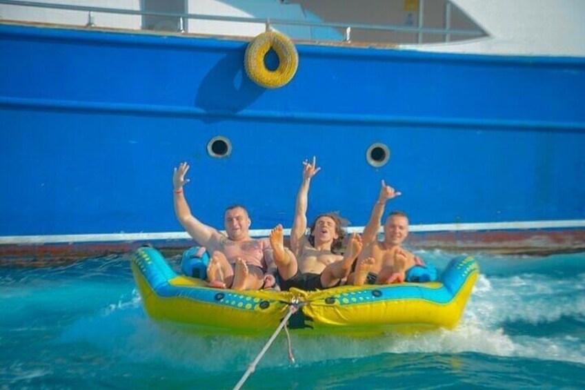 A group of people on a yellow and blue inflatable raft in a pool with a blue boat in the background. 3