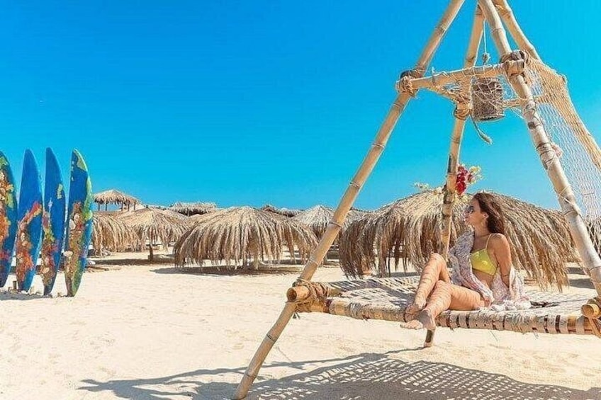 A beach with thatched umbrellas, a hammock, and surfboards. 1