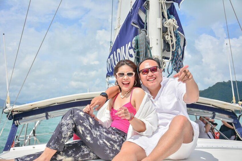 Deux personnes se trouvent à bord d’un voilier à la voile bleue, et un drapeau flotte, sur lequel on peut lire le mot « Voile ». 3