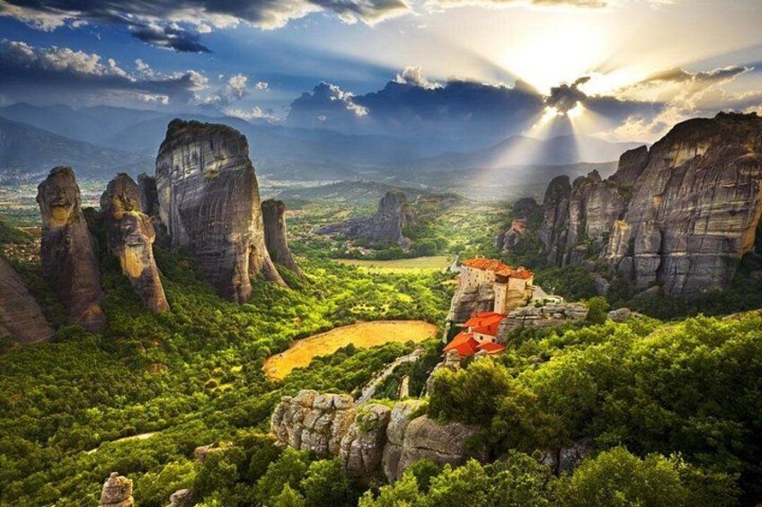 A mountainous landscape with rock formations, a small village with red-roofed buildings, and a valley with greenery. 1
