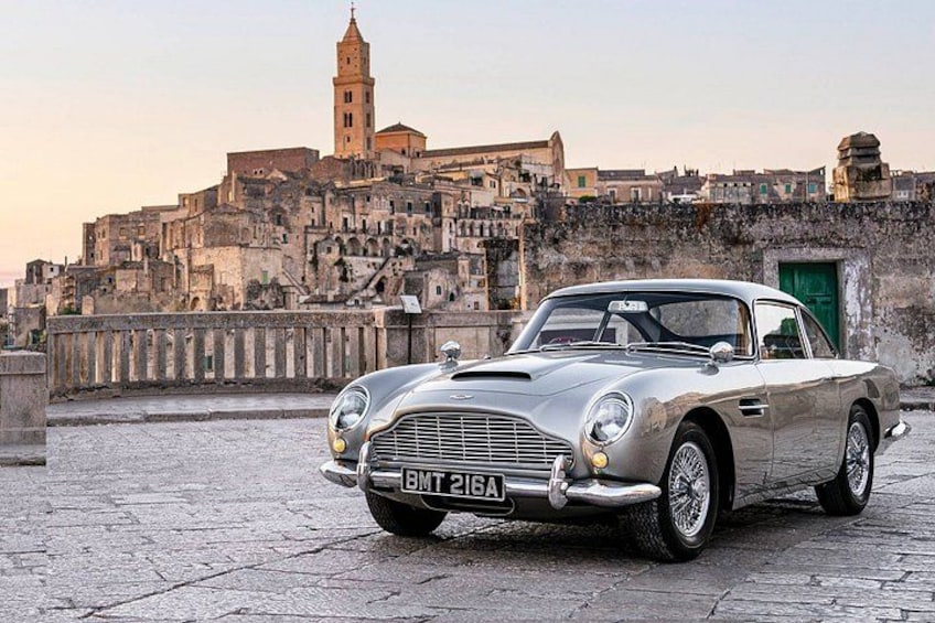 A classic silver sports car parked on a cobblestone street with a historic cityscape in the background. 5