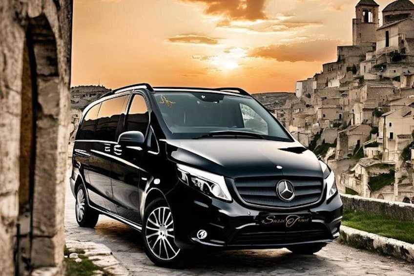 A black Mercedes-Benz Sprinter van parked on a cobblestone path with a historic village and a church in the background. 1