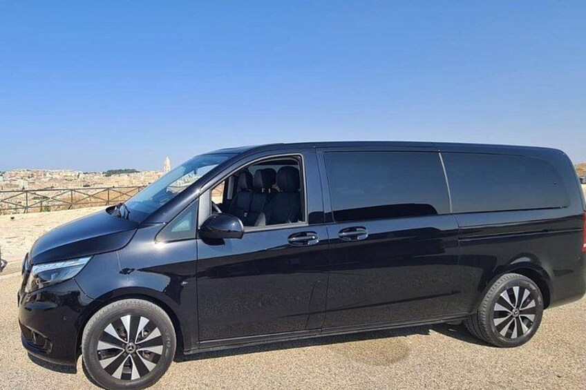 Una camioneta negra estacionada sobre una superficie de grava, con un cielo despejado y edificios lejanos al fondo. 3