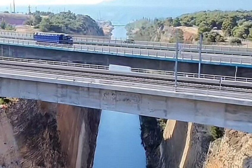 A blue train on a bridge over a river with cliffs and greenery in the background. 3