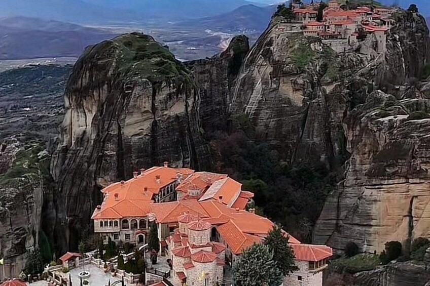 A monastery on a rocky cliff with red-roofed buildings and a panoramic view of the surrounding landscape. 2