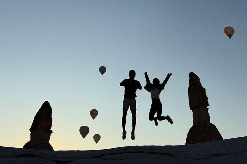 People jumping in the air with hot air balloons in the background. 2