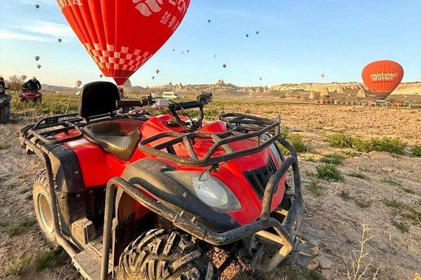 A red ATV in a desert landscape with hot air balloons in the background. 4