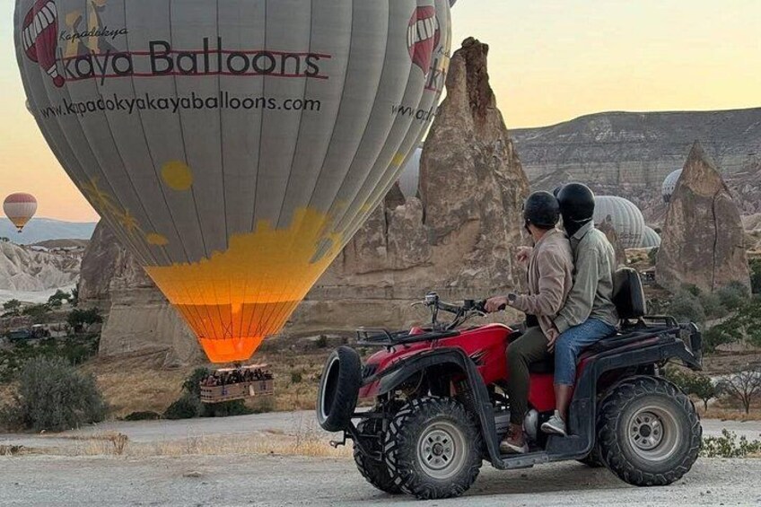 A hot air balloon with the text 'Kaya Balloons' and a website address, a red ATV with two people, and a rocky landscape with unique rock formations in the background. 1