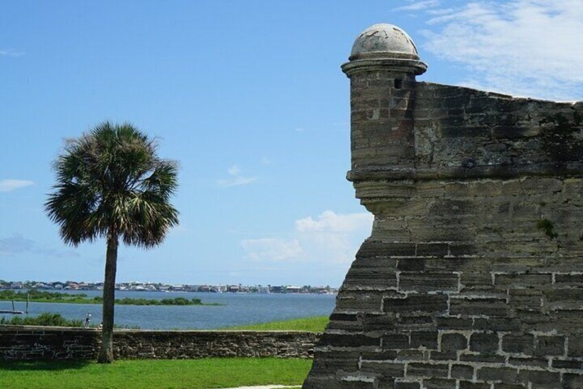 A stone fortification with a palm tree in the foreground and a body of water in the background. 2