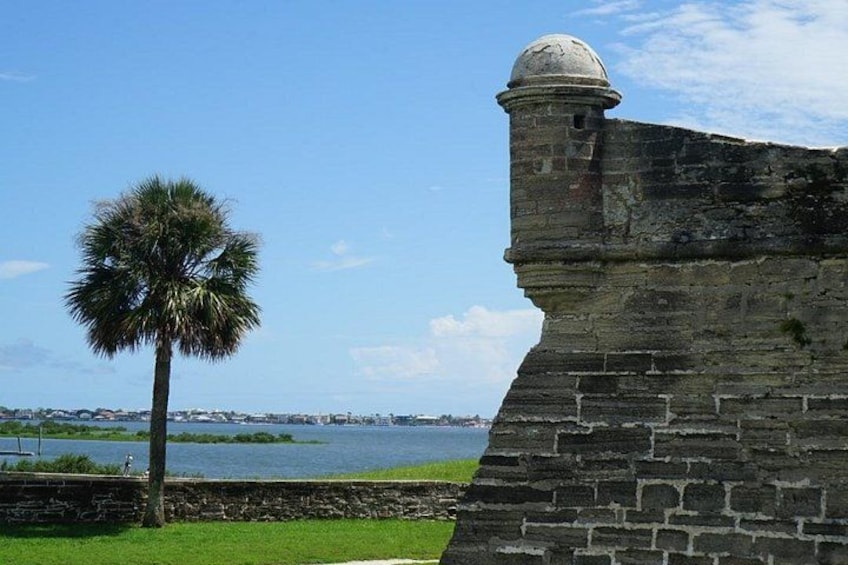 Une fortification en pierre, avec un palmier au premier plan et une étendue d’eau en arrière-plan. 4