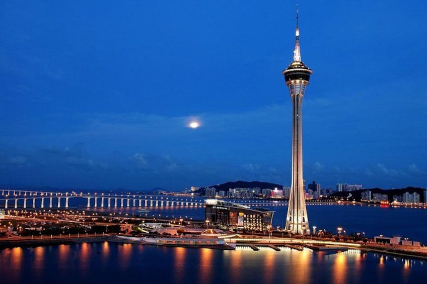 A nighttime cityscape with a prominent tower, a bridge, and a calm body of water reflecting the lights. 5