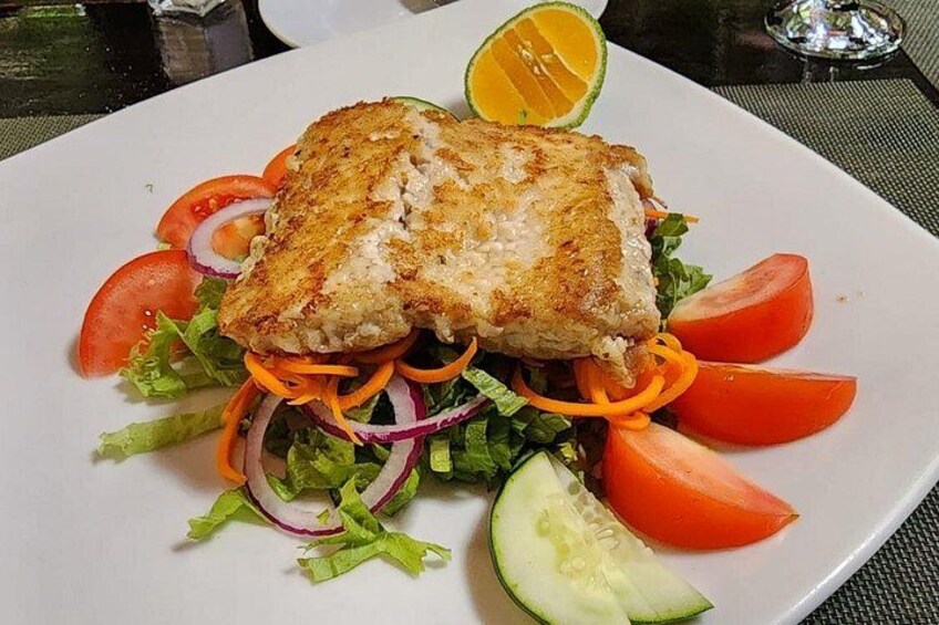 Een bord met een gegrilde vissandwich, salade en een sinaasappelpart. 2