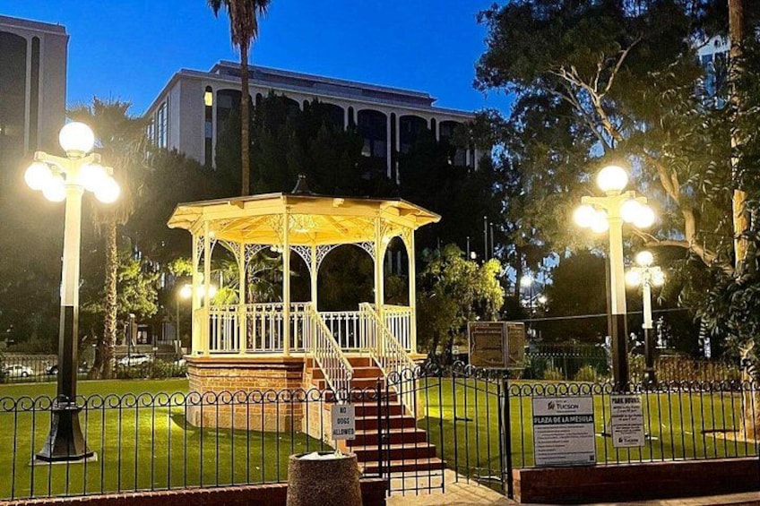 A gazebo with a white railing, surrounded by a fenced area with a grassy lawn, and a building in the background. 3