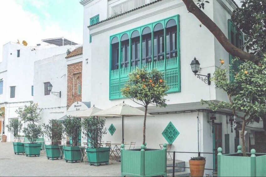 A street with white buildings, green shutters, and potted plants. 3