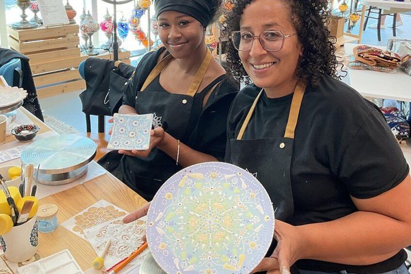 Two people holding patterned plates, with crafting supplies on a table. 2