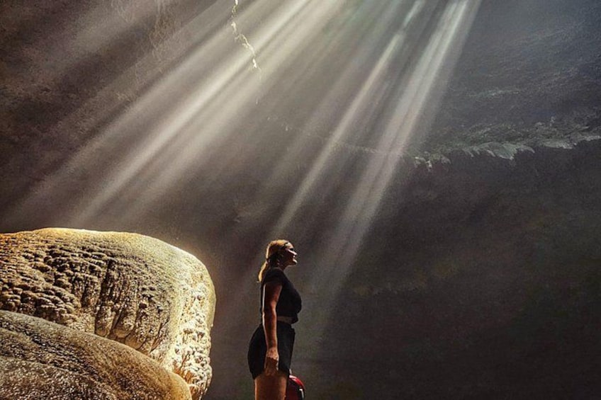 A person standing next to a large rock formation with sunlight streaming through. 1