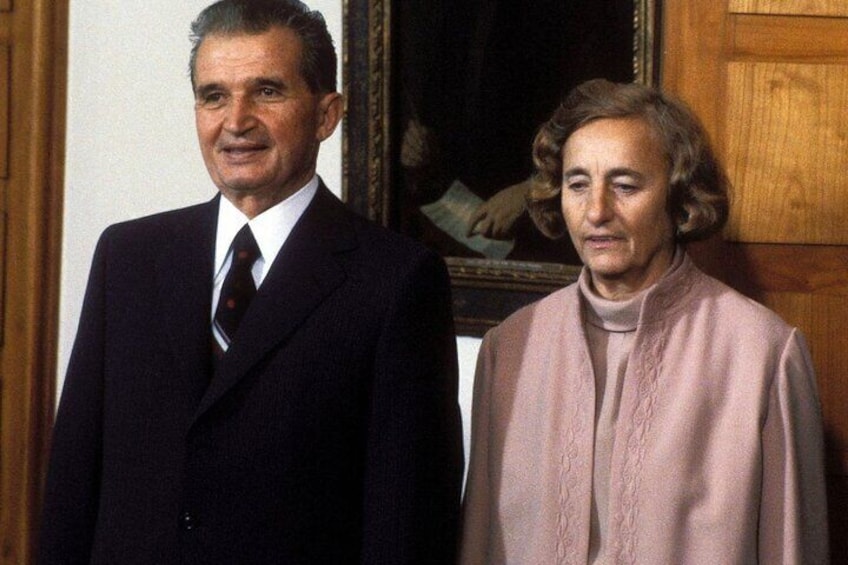 Two people standing in a room with wooden paneling and a framed picture on the wall. 1