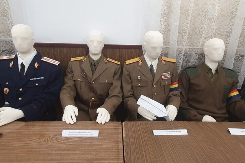 Four mannequins in military uniforms seated at a wooden table with nameplates. 5
