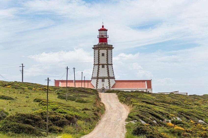 A lighthouse with a red top, a dirt path leading to it, and a building with a red roof in the background. 4