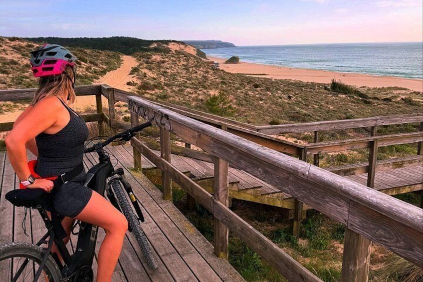 A person on a bicycle on a wooden boardwalk overlooking a beach. 1