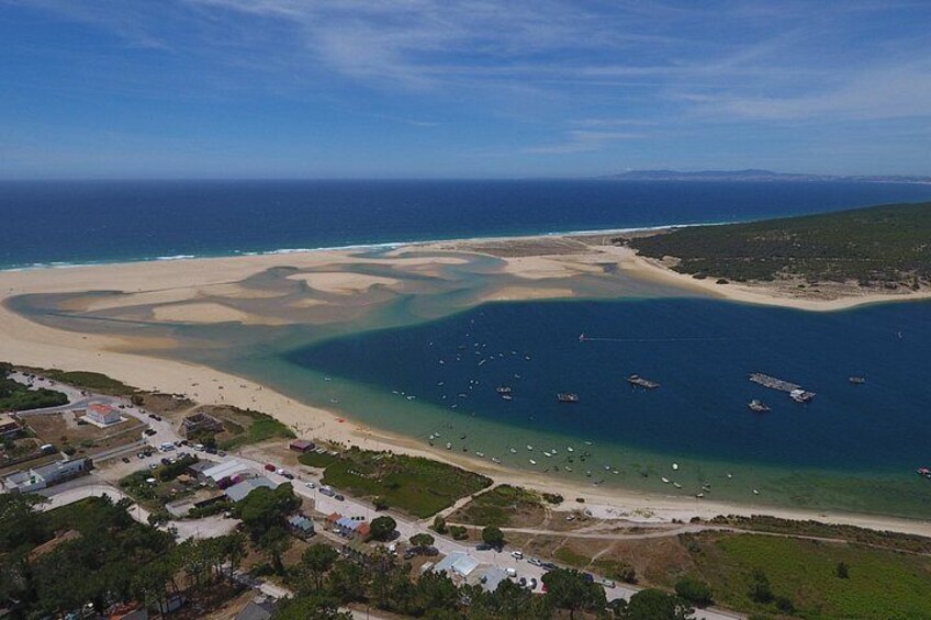 A coastal landscape with a sandy beach, clear blue waters, and boats anchored offshore. 5